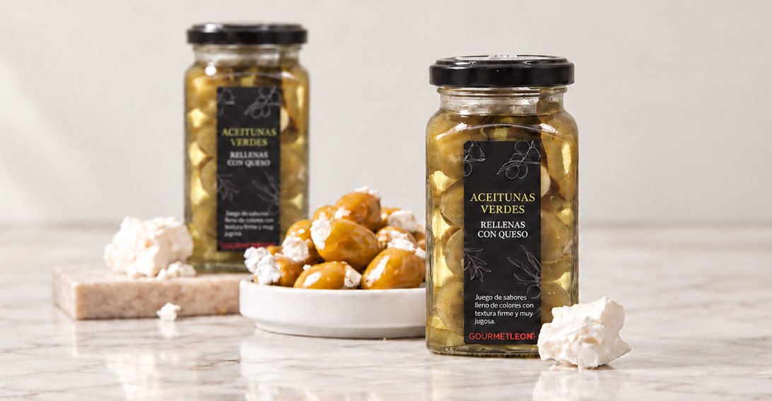 Tarros de aceitunas rellenas de queso Gourmet Leon junto a un plato de aceitunas y queso