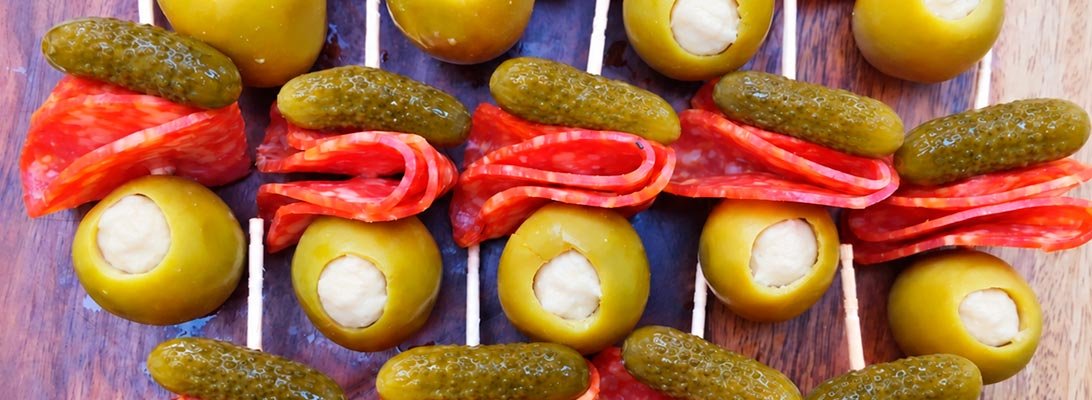 Pinchos de salami con aceitunas verdes rellenas de queso crema y pepinillos sobre una tabla de madera Pinchos de salami con aceitunas verdes rellenas de queso crema y pepinillos sobre una tabla de madera